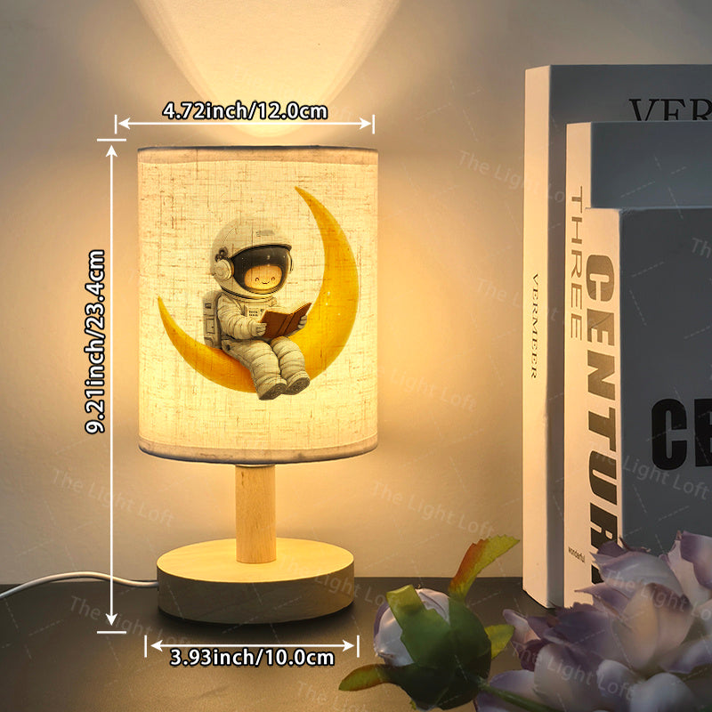Une charmante lampe de chevet LED avec un adorable astronaute de dessin anim assis sur une lune croissante jaune conue pour une ambiance chaleureuse Cette lampe alimente par USB est livre avec un abatjour en tissu et une base en bois nordique